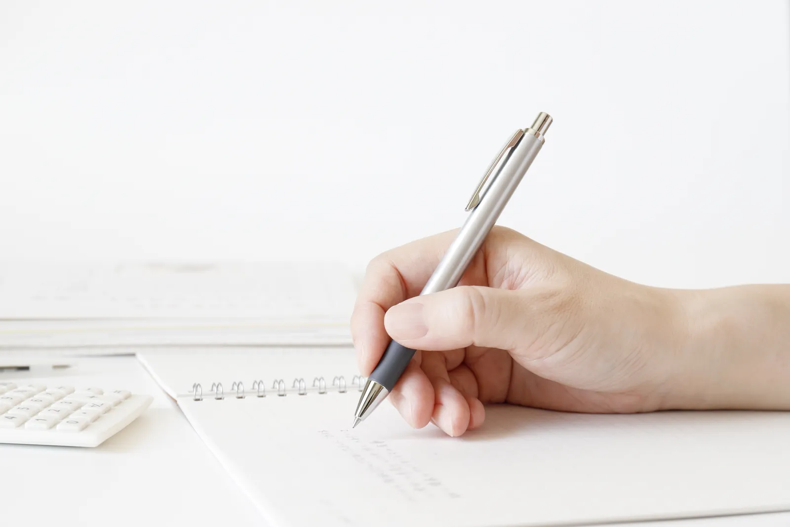 机の上でノートに書き込み、書類を整理する人の手元